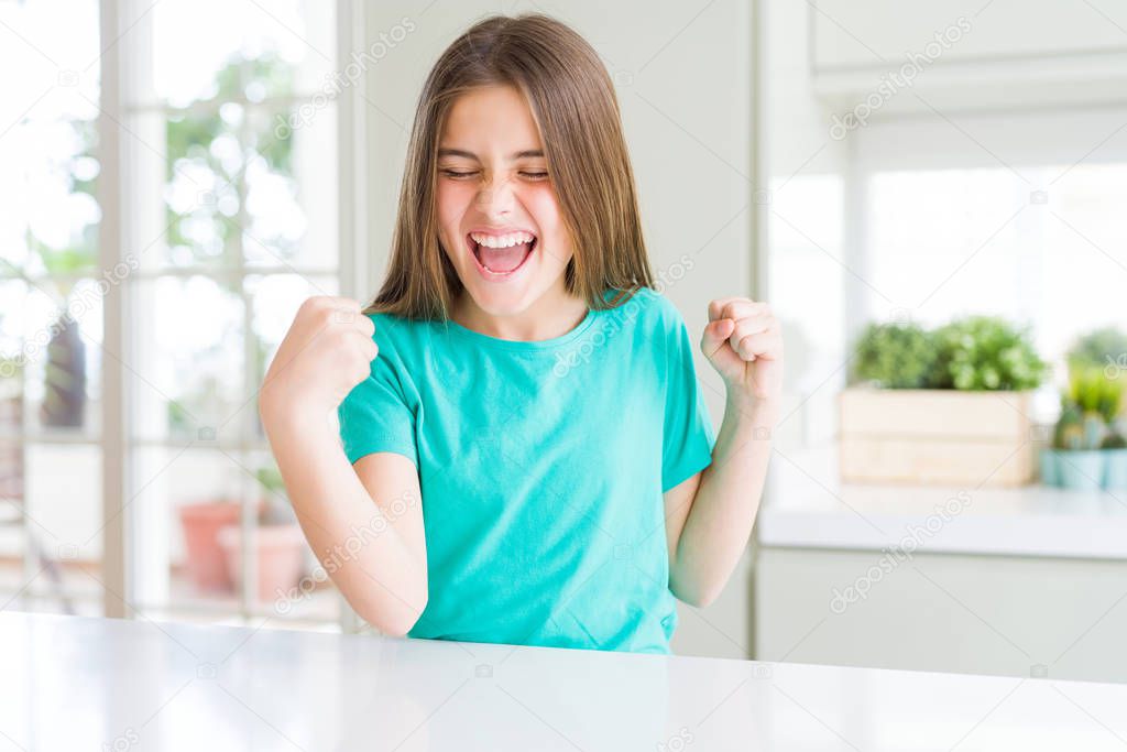 Beautiful young girl kid wearing green t-shirt very happy and excited doing winner gesture with arms raised, smiling and screaming for success. Celebration concept.