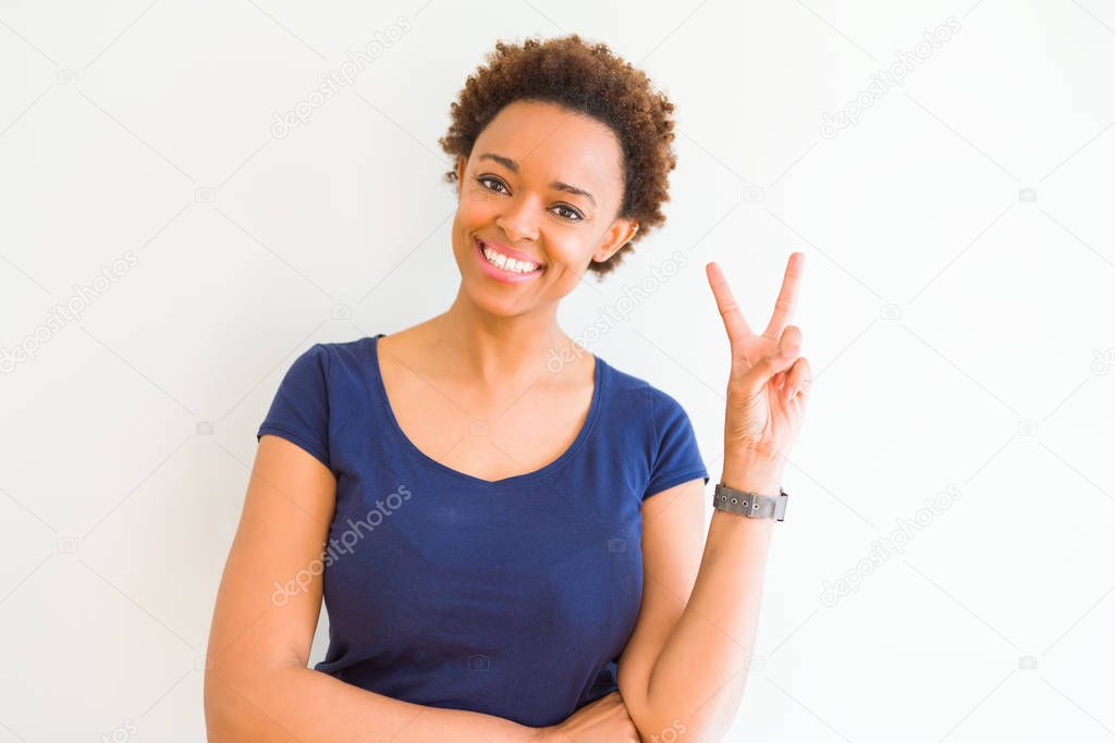 Young beautiful african american woman over white background smiling with happy face winking at the camera doing victory sign. Number two.