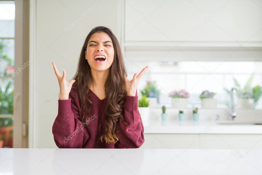 Young beautiful woman at home crazy and mad shouting and yelling with aggressive expression and arms raised. Frustration concept.