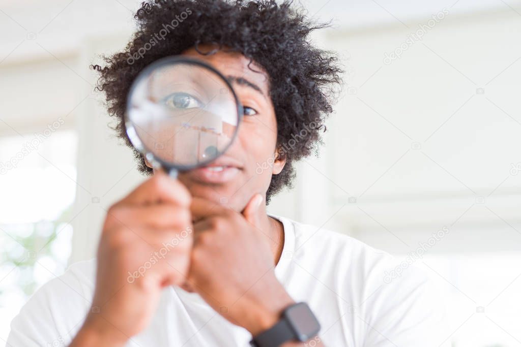 African American man looking through magnifying glass serious face thinking about question, very confused idea