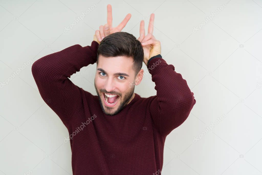 Young handsome man wearing a sweater over isolated background Posing funny and crazy with fingers on head as bunny ears, smiling cheerful