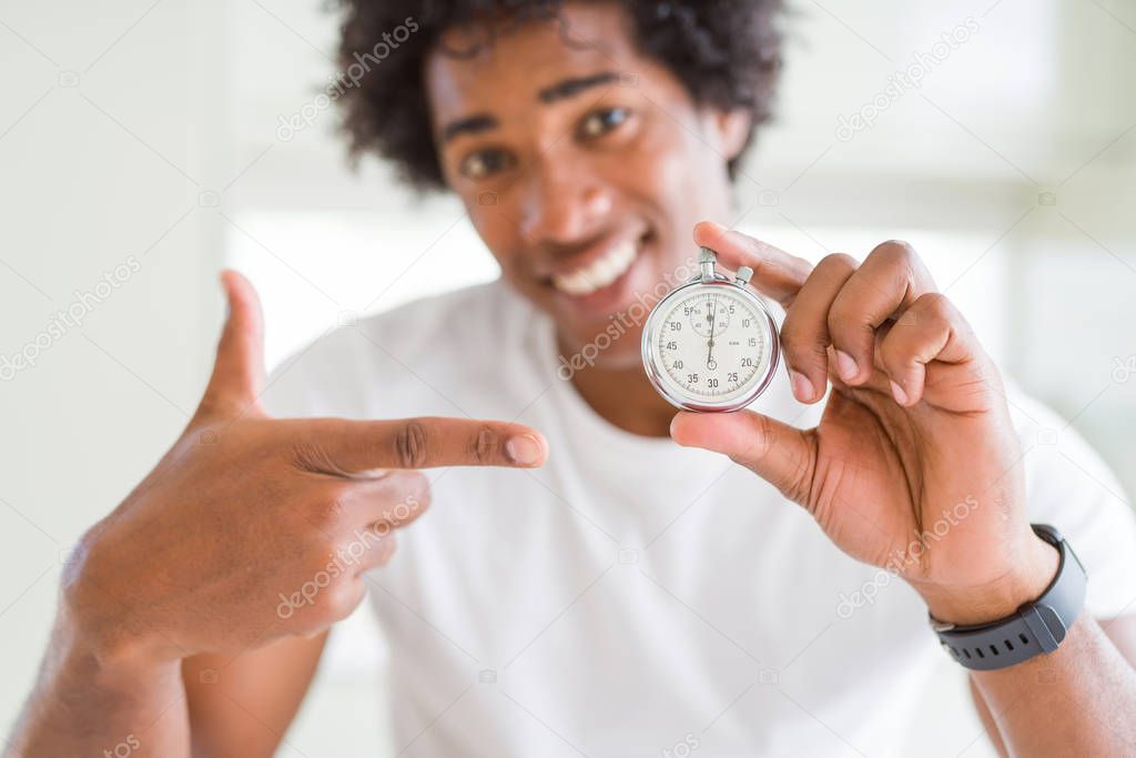 African American man holding stopwatch very happy pointing with hand and finger