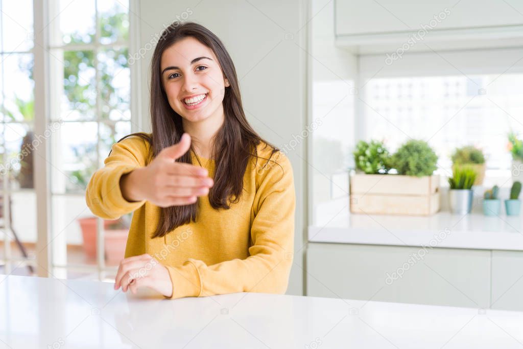 Beautiful young woman wearing yellow sweater smiling friendly offering handshake as greeting and welcoming. Successful business.
