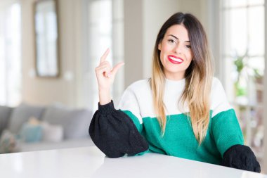 Kış kazak evde gülümseyen ve kendine güvenen giyen genç güzel kadın boyutu işaret parmaklı ararken ve kamera işi el ile el hareketi. Ölçü kavramı.