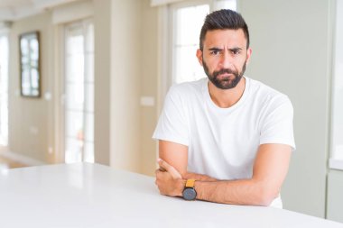 Yakışıklı İspanyol ev şüpheci ve sinir, onaylamayan ifade yüz çapraz kolları üzerinde rahat beyaz t-shirt dostum. Negatif kişi.
