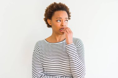 Stresli ve gergin elle çivi ısırma ağzına bakarak beyaz arka plan üzerinde çizgili Süveter giyen genç güzel Afrikalı-Amerikalı kadın. Anksiyete sorunu.