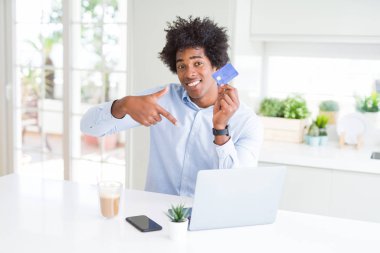 Afrika kökenli Amerikalı adam dizüstü kullanarak ve sürpriz yüz işaret parmağı kendisine kredi kartıyla alışveriş online