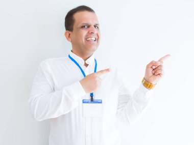 Orta yaş iş adamı gülümseyen ve iki elleri ve parmakları ile tarafına işaret kamera bakıyor beyaz arka plan üzerinde kimlik kartı takıyor.