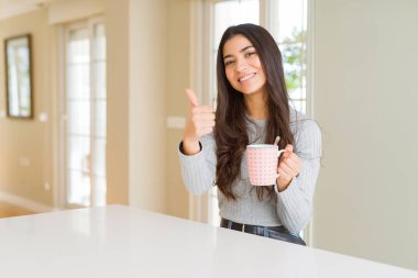 Genç kadın bir fincan kahve mutlu ok işareti, başparmak ile parmak, mükemmel işareti yapıyor kocaman bir gülümseme ile içme