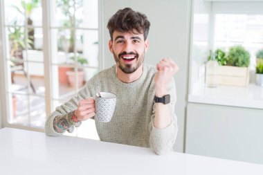 Genç adam gurur çığlık ve zafer ve başarı çok heyecanlı, kutlama sabah bir fincan kahve içme duygu tezahürat