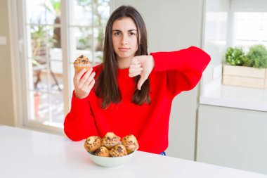 Güzel ve genç birbayan yeme çikolata muffins kızgın yüzü, eksi işareti aşağı antipati başparmak ile gösterilen, ret kavramı ile cips