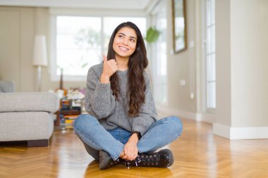 Evde katta oturan genç güzel kadın hareketi el ile mutlu Yaşasın yapıyor. Kameraya bakarak başarı gösteren ile ifade onaylama.