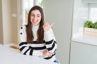 Seyir ve başparmak yanında yukarıyı mutlu yüz ile gülümseyen çizgili Süveter giyen güzel genç kadın.