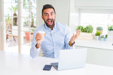 İspanyol yakışıklı çalışma kullanma bilgisayar dizüstü bilgisayar ve bir fincan kahve çok mutlu ve heyecanlı, kazanan ifade ile büyük çığlık zaferini kutluyor içme gülümse ve el kaldırdı