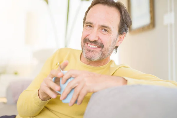 ハンサムな中年男がソファーに座ってリラックス コーヒーを一杯飲み 自宅のカメラで笑顔 — ストック写真