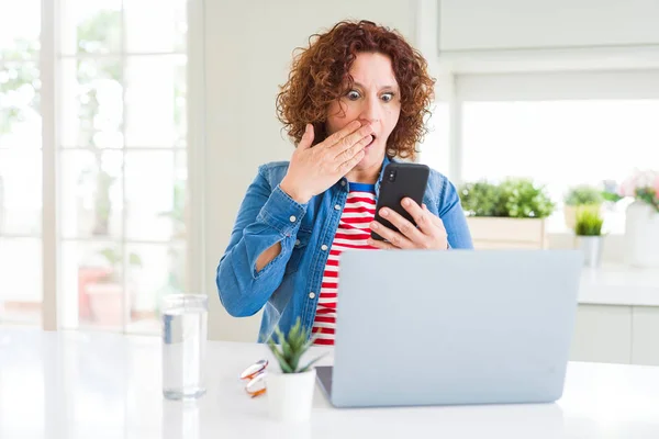Ανώτερος Γυναίκα Χρησιμοποιώντας Laptop Και Smartphone Κάλυμμα Στόματος Χέρι Σοκαρισμένος — Φωτογραφία Αρχείου