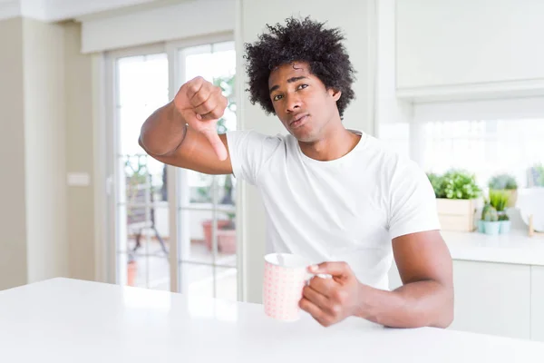 African American man with afro hair drinking a cup of coffee with angry face, negative sign showing dislike with thumbs down, rejection concept