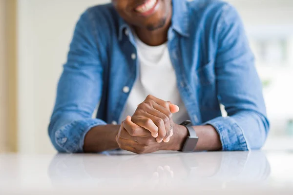 Close up of crossed hands of african man over table smiling