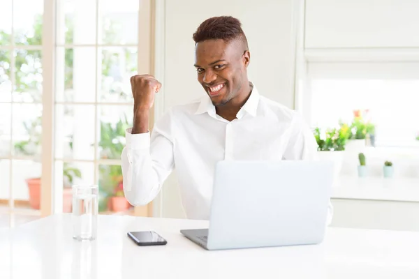 アフリカ系アメリカ人ビジネスの男性を探していると親指側に上向きの幸せそうな顔を浮かべてラップトップを使用して作業 — ストック写真