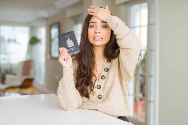 Young woman holding passport of Canada stressed with hand on head, shocked with shame and surprise face, angry and frustrated. Fear and upset for mistake.