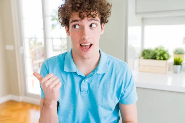 カジュアルなブルー シャツを着て家で若いハンサムな男を浮かべて幸せそうな顔見ると側を親指で指す — ストック写真