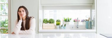 Güzel genç kadın masada düşünme seyir yorgun ve çapraz kolları olan depresyon sorunları ile sıkılmış beyaz evde oturan geniş açı resim.