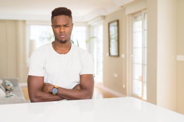 Afro-Amerikan yakışıklı beyaz masa evde şüpheci ve sinir, onaylamayan ifade yüz çapraz kolları üzerinde. Negatif kişi.