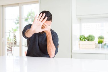 Evde rahat kazak giyen yakışıklı İspanyol adam elleriyle gözlerini kapsayan ve stop yapıyor jest ile üzgün ve korku ifadesi. Utandım ve negatif kavramı.