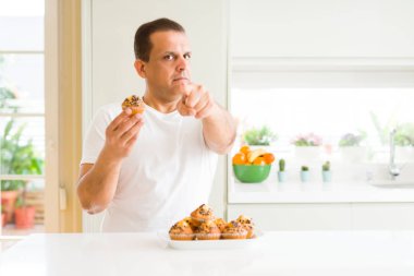 Orta yaş adam yeme Çikolatalı kekler evde el işareti, pozitif ve kendinden emin bir jest ön kamera ve size, parmak ile işaret