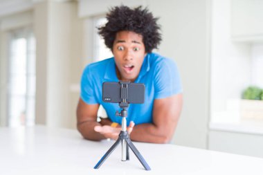 Bir sürpriz yüz, korkuyor ve heyecanlı korku ifadesi ile smartphone şokta korktuğunu kullanarak web kamerası ile online arama yapan Afro-Amerikan erkek