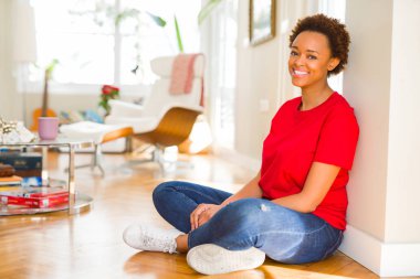 Kamera yere evde oturmak diş gösteren emin gülümseyen güzel genç Afro-Amerikan kadın