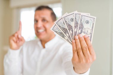 Orta yaş erkek tutan dolar bir fikirle sürpriz bir sürü ya da gülen yüz, bir numara ile işaret parmağı soru