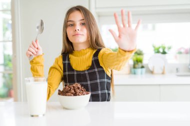 Güzel genç kız çocuk çikolata Hububat ve bardak süt için açık eliyle dur işareti ile ciddi ve kendine güvenen ifade, savunma jest yapıyor Kahvaltı