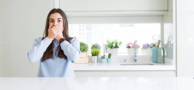 Güzel genç kadın evde beyaz masaya oturan geniş açı resim kaplama ağız elle hata için şok. Gizli kavramı.