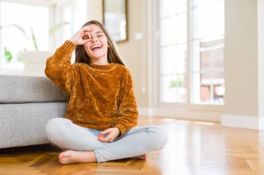 Güzel genç kız çocuğun evde katta oturan gülümsüyor, parmakları ile mutlu yüz üzerinden seyir göz el ile ok jest işi.