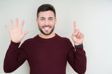 Gösterilen ve parmakları ile işaret izole arka plan üzerinde bir kazak giyen genç yakışıklı adam kendinden emin ve mutlu gülümseyerek süre 6 numara.