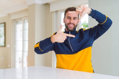 Yakışıklı adam evde elleriyle yapım çerçeve ve parmakları ile mutlu yüz gülümsemeye. Yaratıcılık ve Fotoğrafçılık kavramı.