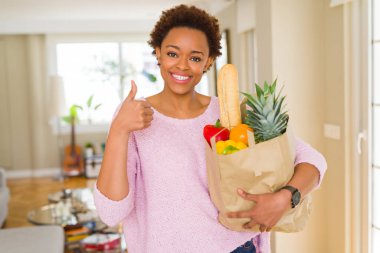 Ok işareti, başparmak ile parmak, mükemmel işareti yapıyor kocaman bir gülümseme ile kağıt torba taze yiyecek dolu mutlu tutan genç Afro-Amerikan kadın