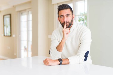 Evde rahat beyaz kazak giyen İspanyol yakışıklı dudaklarında parmak ile sessiz olmanı. Sessizlik ve gizli kavramı.