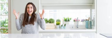 Güzel genç kadın evde beyaz masaya oturan geniş açı resim çılgın ve başarı için hayran kaldırdı Kollarını açarak kutluyor ve heyecanlı çığlık gözleri açık. Kazanan kavramı