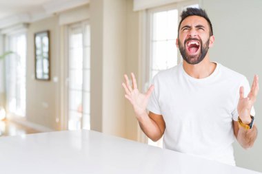 Yakışıklı İspanyol adam rahat beyaz t-shirt evde çılgın ve kızgın bağırarak ve agresif ifade ve silah ile bağırmaya kaldırdı. Hayal kırıklığı kavramı.
