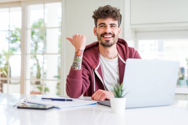 Bilgisayar laptop ve işaret ve başparmak kadar mutlu yüz gülümseyen tarafı ile gösterilen defter kullanan genç öğrenci adam