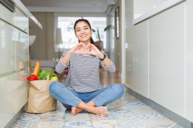 Mutfakta taze yiyecek aşık kalp simgesi ve elleriyle şekil gösteren gülümseyen dolu kese kağıdı ile oturan bir genç bayan. Romantik kavramı.
