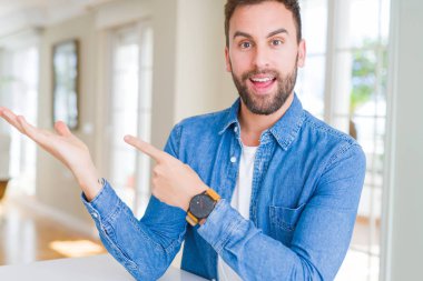 Yakışıklı adam evde hayret ve gülümseyerek kameraya el ile sunulması ve ile işaret parmak iken.
