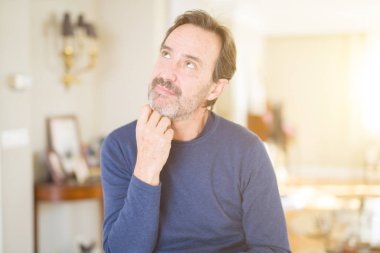 Yakışıklı orta yaş erkek evde ile el çeneme soru dalgın ifade hakkında düşünme. Düşünceli yüzüyle gülümsüyor. Şüphe kavramı.