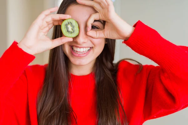 美丽的年轻女子吃半新鲜的绿色猕猴桃与快乐的脸微笑做确定的标志与眼睛看着通过手指 — 图库照片