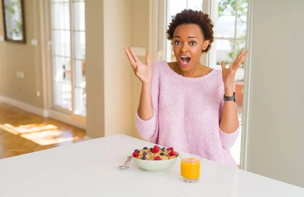 年轻的非洲裔美国妇女在早上在家里吃健康的早餐庆祝疯狂和惊讶的成功与手臂抬起和睁开眼睛尖叫兴奋 优胜者概念 — 图库照片