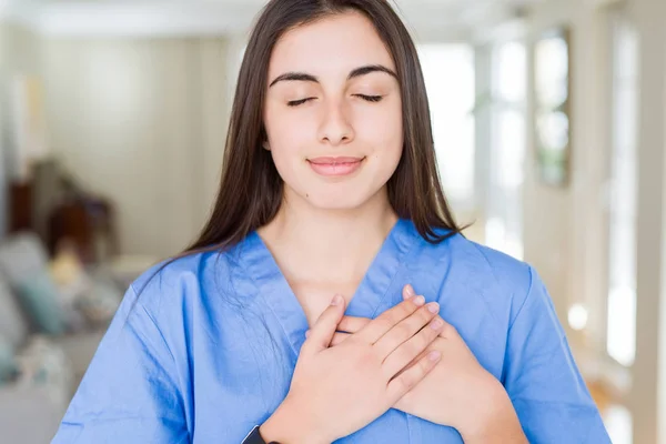 Bela Jovem Enfermeira Clínica Sorrindo Com Mãos Peito Com Olhos — Fotografia de Stock