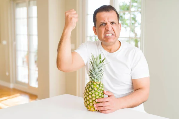 中年男子吃新鲜的热带菠萝在家里恼火和沮丧的喊声与愤怒 疯狂和大喊大叫与提高的手 愤怒的概念 — 图库照片