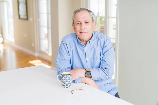 Handsome senior man drinking a cup of coffee at home with a happy and cool smile on face. Lucky person.